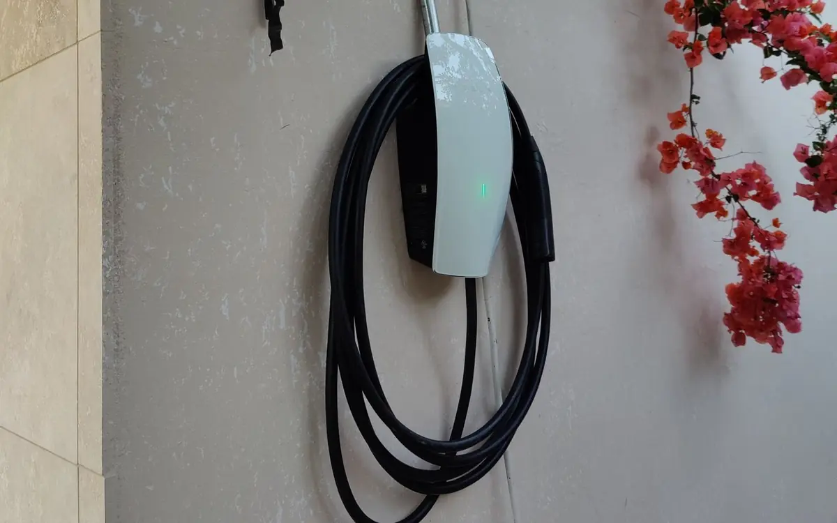 Tesla Wall Connector installed on an exterior wall with conduit, framed by bougainvillea