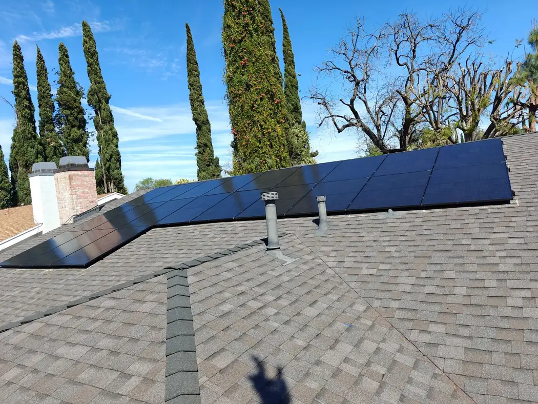 Black solar panels on a gray shingle roof under a blue sky