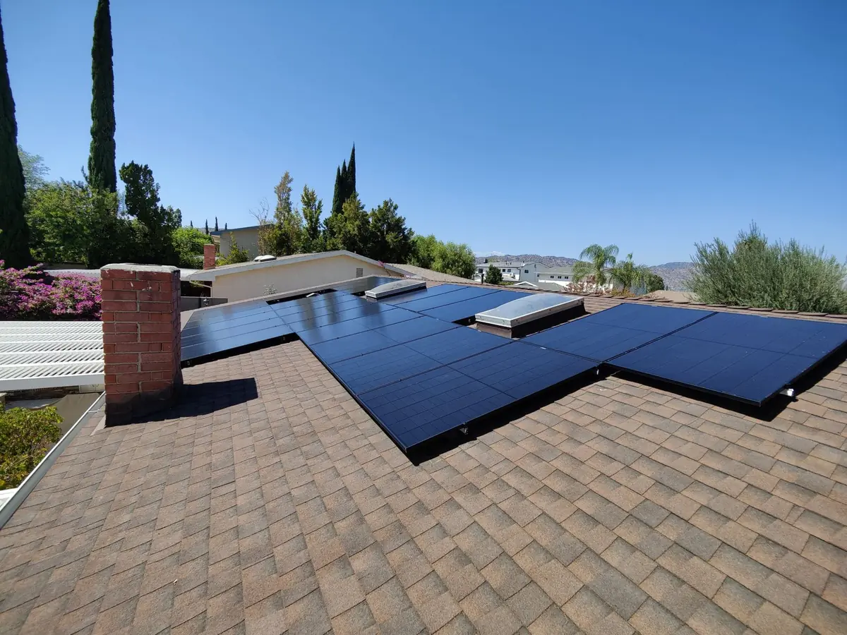 Black solar panels installed around two skylights on a shingle roof